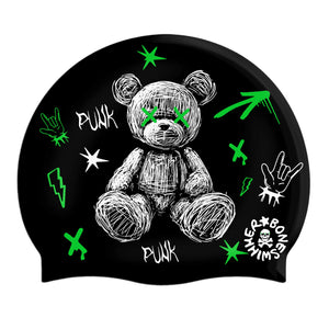 Cuffia da piscina in silicone spessorato, modello Psycho Boneswimmer con base colore nero e grafica con un simpatico orsacchiotto disegnato al tratto bianco su un fondo nero circondato da segni e tratti verde fluo, in uno stile un po' acid punk.